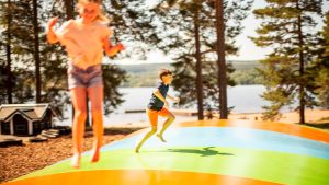 Exempel på aktivitet för barn i Dalarna.Två barn studsar på en hoppkudde, i bakgrunden tallar och sjön Siljan.